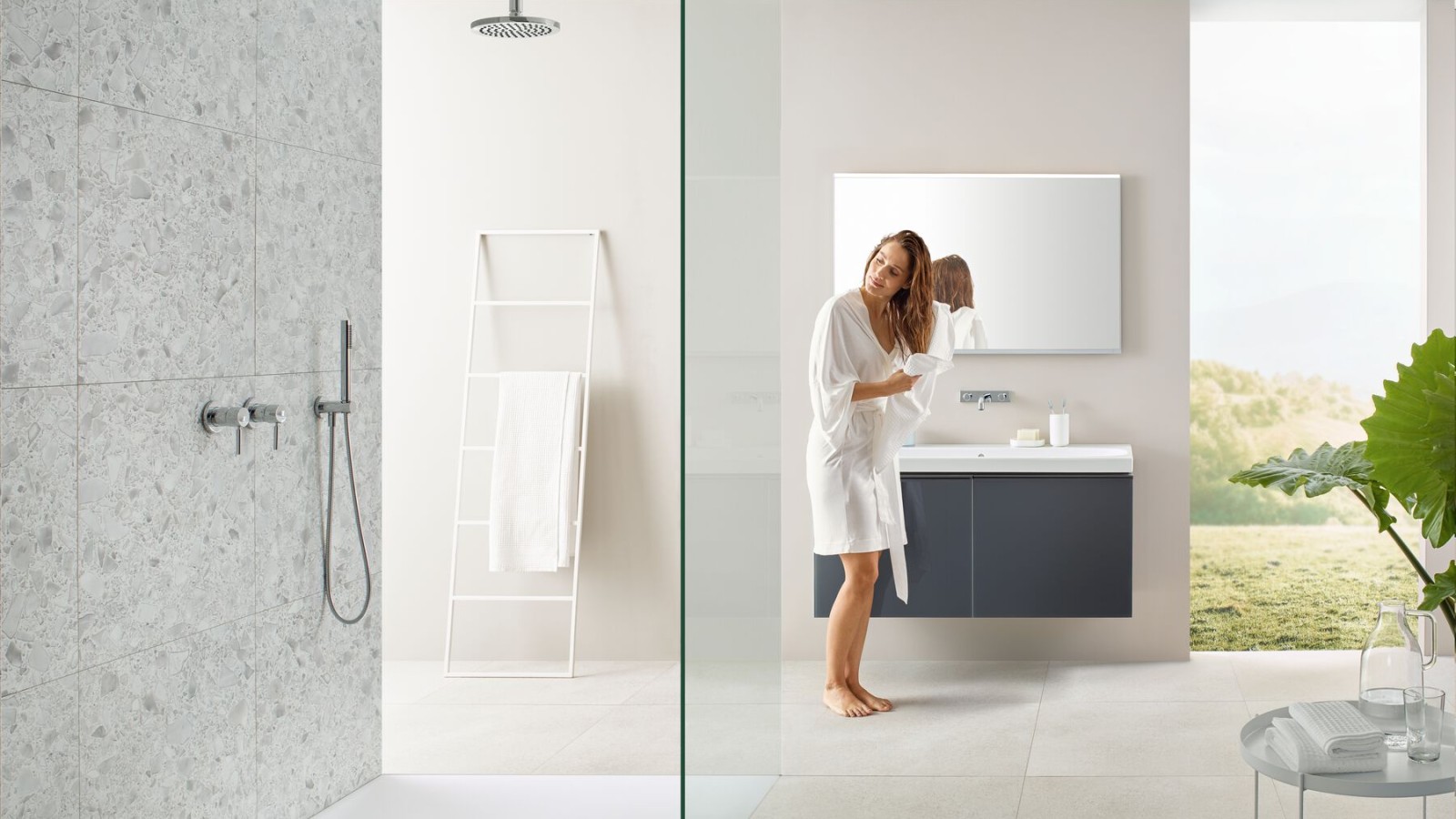 Femme se séchant les cheveux avec une serviette dans une salle de bains avec douche ouverte et grands carreaux de style terrazzo Femme se séchant les cheveux avec une serviette dans une salle de bains avec douche ouverte et grands carreaux de style terrazzo