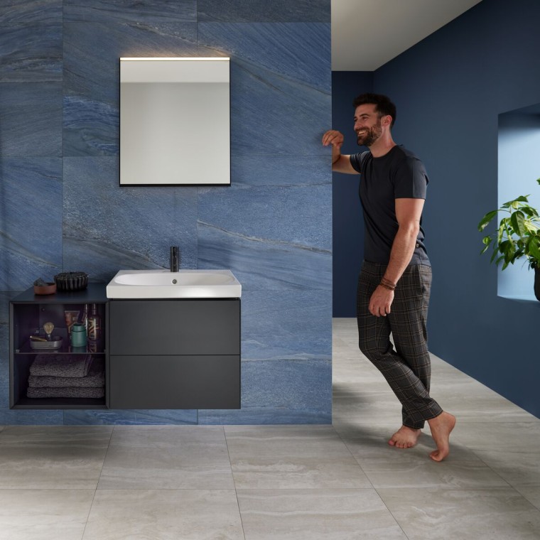 Homme adossé au mur dans une salle de bains bleue avec un lavabo Geberit Mix & Match Homme adossé au mur dans une salle de bains bleue avec un lavabo Geberit Mix & Match