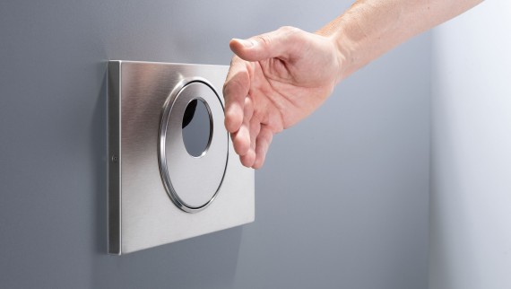 Une main est placée devant la plaque de déclenchement sans contact Geberit Sigma10 round avec commande déportée Une main est placée devant la plaque de déclenchement sans contact Geberit Sigma10 round avec commande déportée