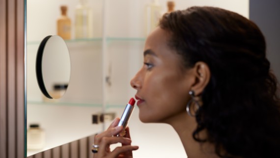 Femme se passant du rouge à lèvres devant un miroir grossissant (© Geberit)