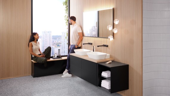 Une femme et un homme dans une grande salle de bains équipée d’un lavabo double Geberit ONE, d’un miroir Option et d’éléments en bois Une femme et un homme dans une grande salle de bains équipée d’un lavabo double Geberit ONE, d’un miroir Option et d’éléments en bois