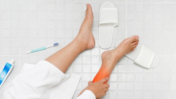 Une femme se tient le pied après avoir glissé sur le sol de la salle de bain* Une femme se tient le pied après avoir glissé sur le sol de la salle de bain*