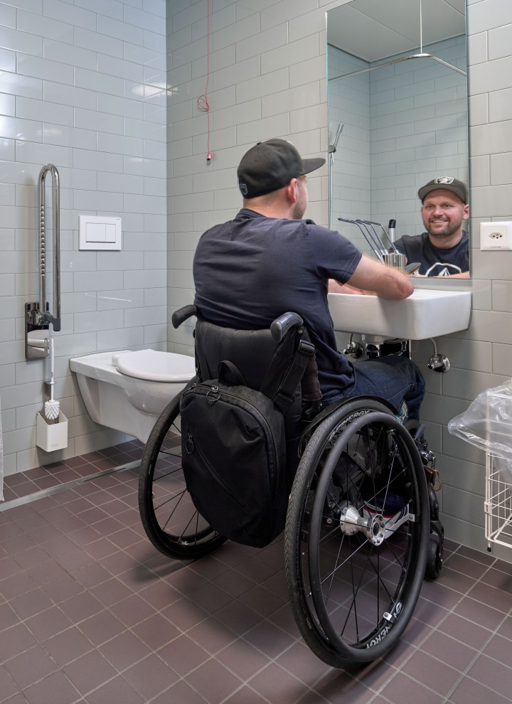 Peter Roos en fauteuil roulant au niveau de la zone de lavage dans une salle de bains adaptée PMR (© Ben Huggler)