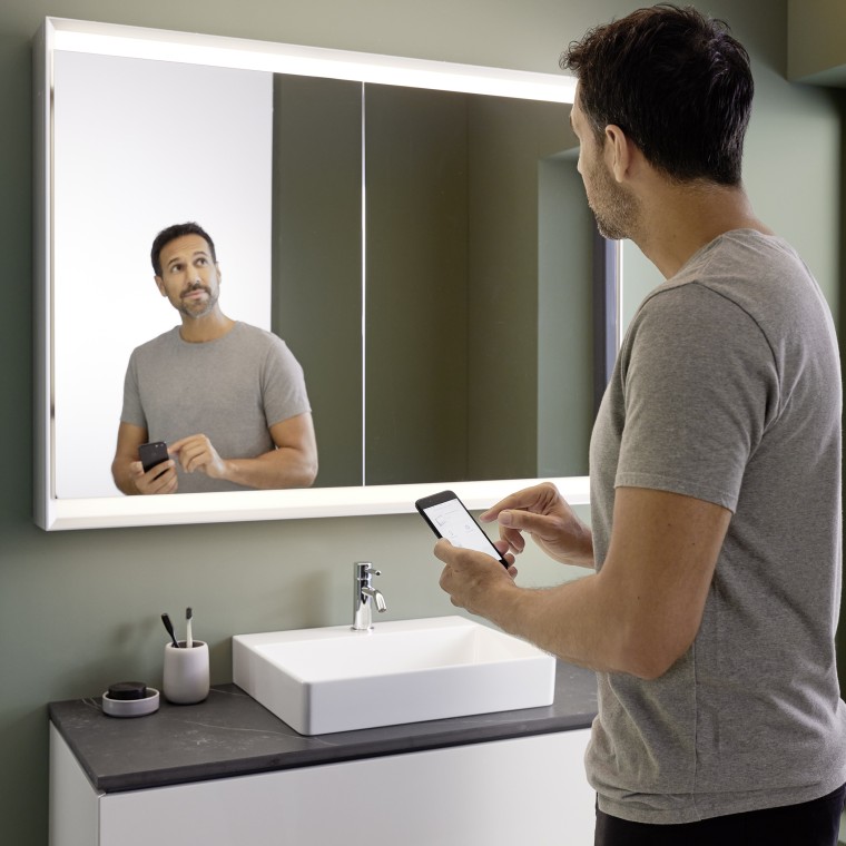 Un homme commande lʼéclairage de lʼarmoire à miroir Geberit ONE avec son smartphone (© Geberit) Un homme commande lʼéclairage de lʼarmoire à miroir Geberit ONE avec son smartphone (© Geberit)